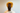 A woman with long, wavy brown hair tied up in a ponytail using ATHENA NEWTON's Luxurious Silk Oversized Scrunchie in Golden Mustard wears a light shirt. The scrunchie adds a bright accent to her hairstyle against the plain backdrop.