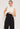 Against a plain background, a person wears a stylish, minimalist outfit featuring ATHENA NEWTON's sleeveless white turtleneck paired with Wrinkle Free Retro Style Pants in black. They adjust the waistband of their high-waisted pants confidently.