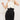 With slicked-back hair, a person wears a white sleeveless turtleneck and ATHENA NEWTON's Wrinkle Free Retro Style Pants in black, featuring smooth gabardine and an asymmetrical wrap detail, posing against a plain background.